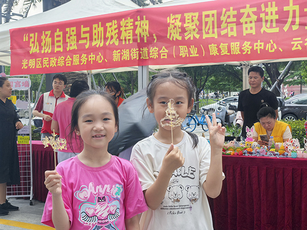 图：小朋友开心展示自制的助残主题糖画作品