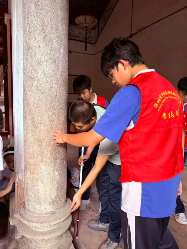 学生志愿者引导盲人抚过斑驳老墙